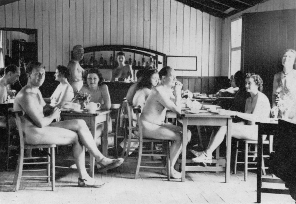 A group of men and women sitting nude in a café. Featured in Nudism in a Cold Climate.